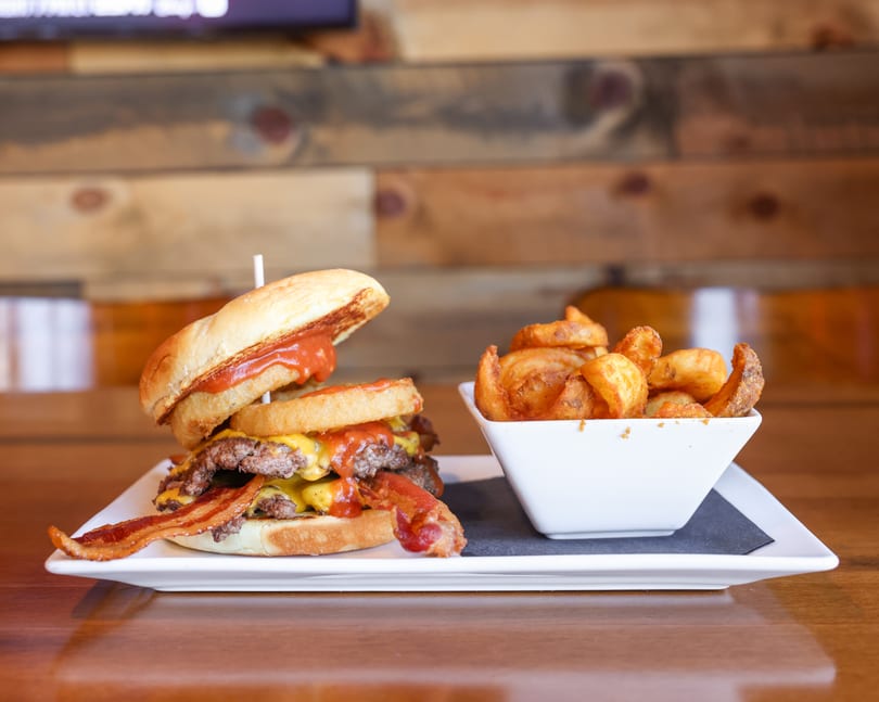 Double cheeseburger with bacon and onion rings, served with a side of potato wedges.