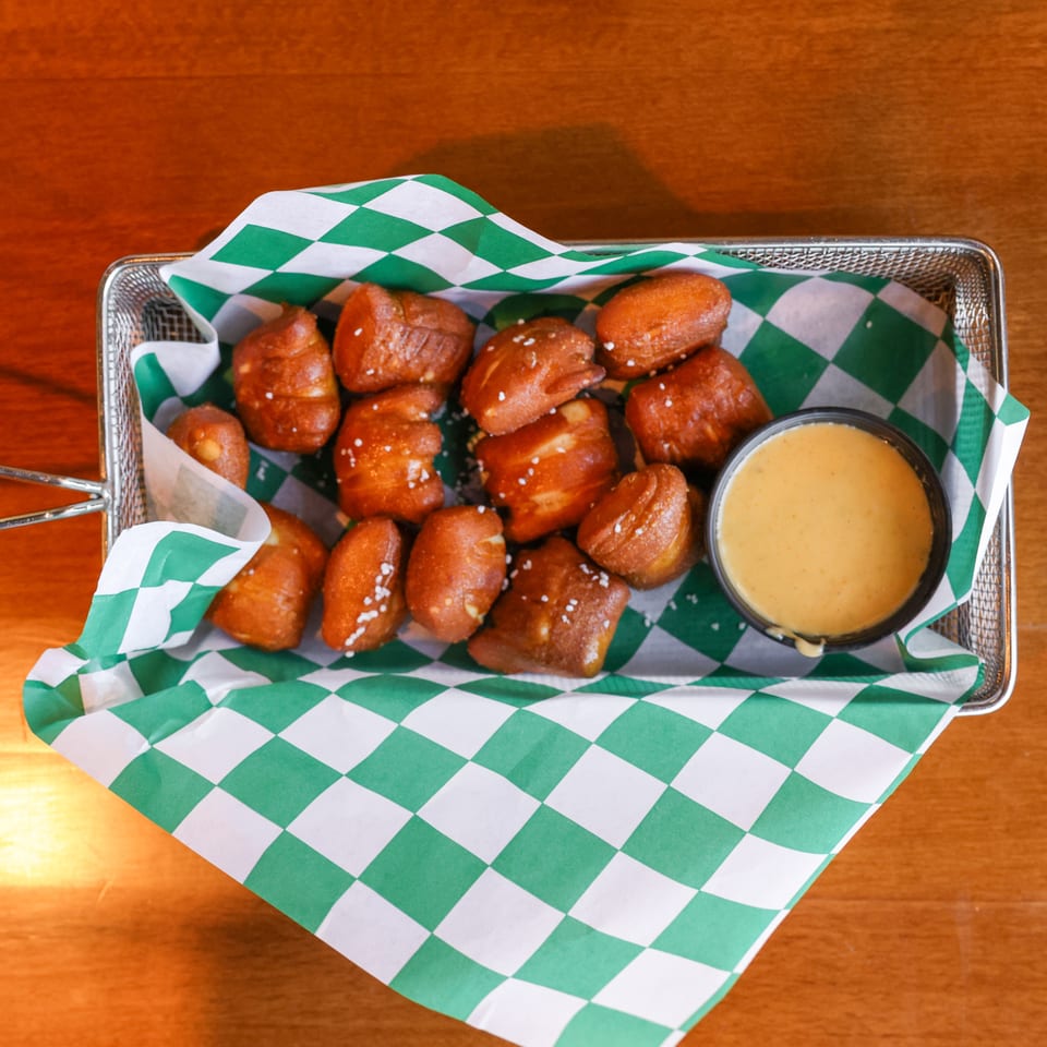 Pretzel bites with salt and a side of cheese dip in a metal basket with green and white checkered paper.