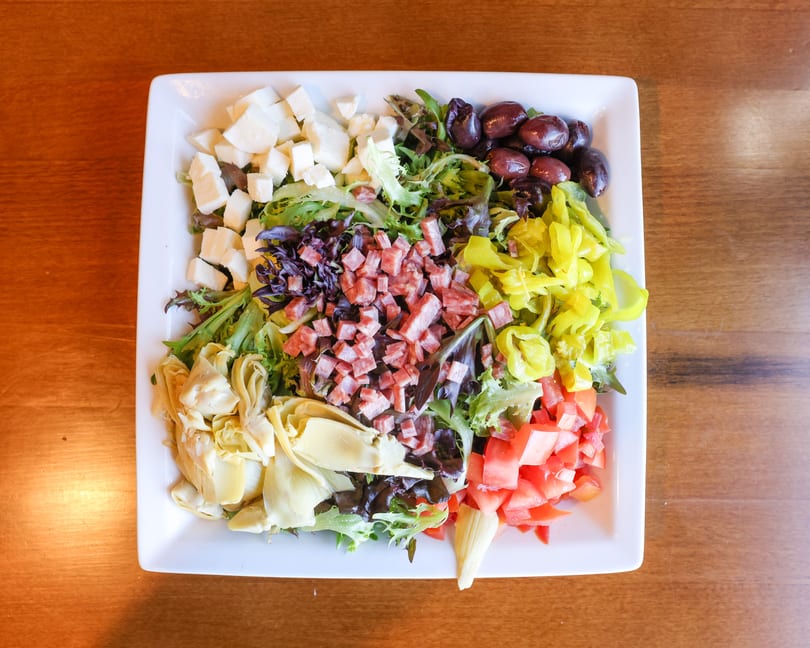 Overhead view of a large salad with cheese, olives, pepperoni, peppers, tomatoes, and artichokes.