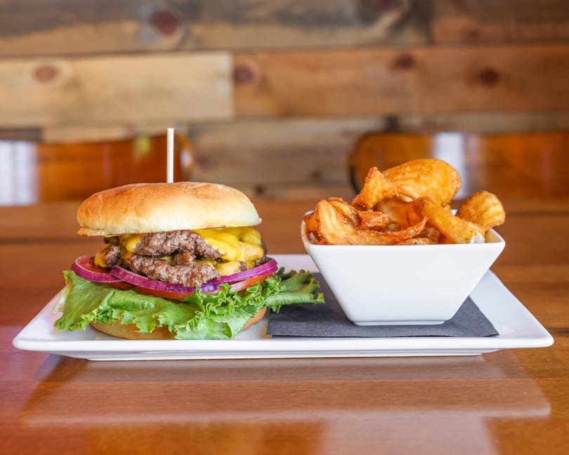 Double cheeseburger with lettuce, tomato, and onion, served with a side of crispy potato wedges.
