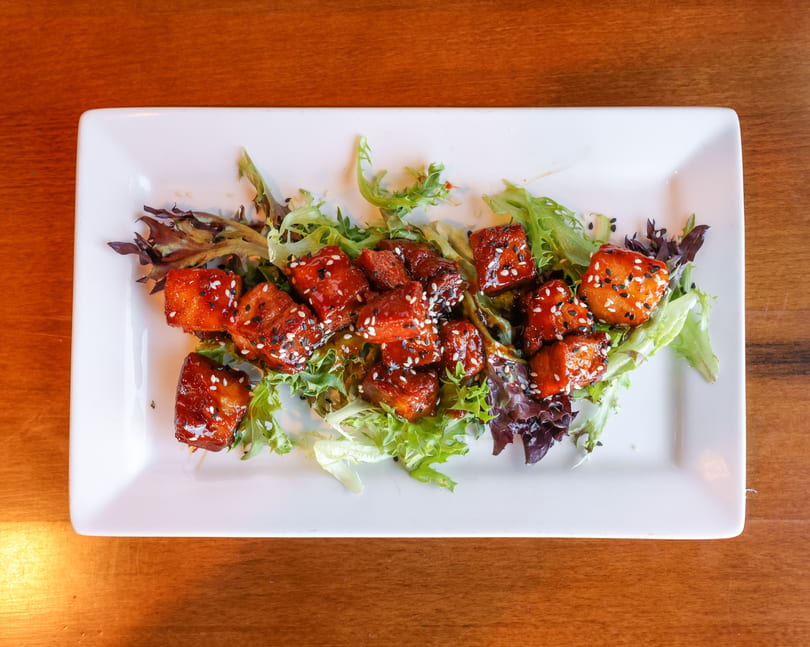 Sweet and sour pork belly bites with sesame seeds on a bed of mixed greens.